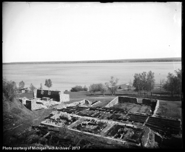 Image of stone ruins with collapsed roof timbers and a placid lake beyond