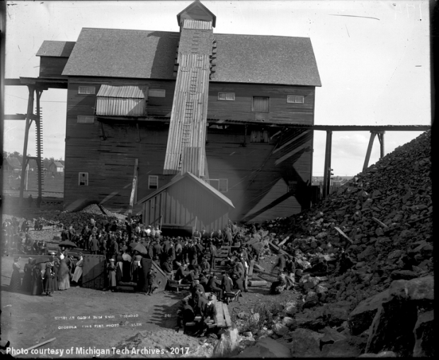 Group of people gathered around a wooden shafthouse